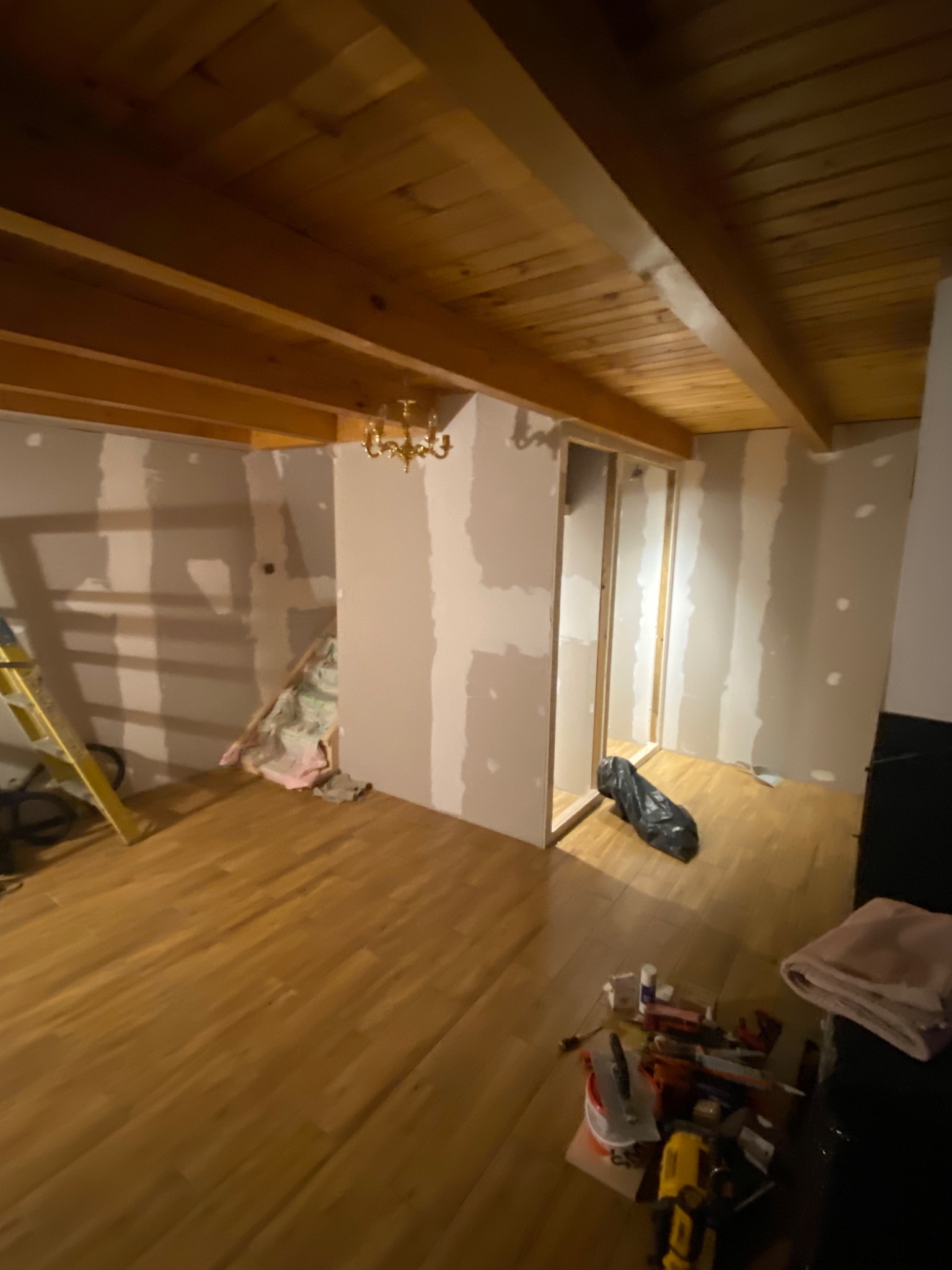 Wnętrze w trakcie prac wykończeniowych: drewniany sufit, ściany przygotowane do malowania, widoczna drabina, narzędzia i materiały budowlane porozrzucane na podłodze.