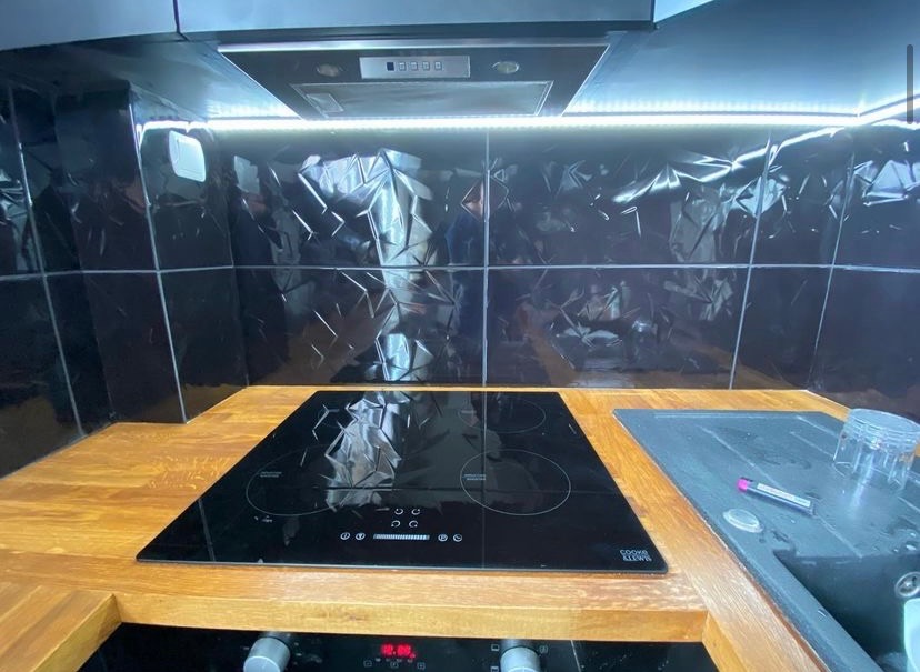 Nowoczesna kuchnia z czarnymi, teksturowanymi płytkami na ścianie, drewnianym blatem i czarną płytą indukcyjną Cook & Lewis.