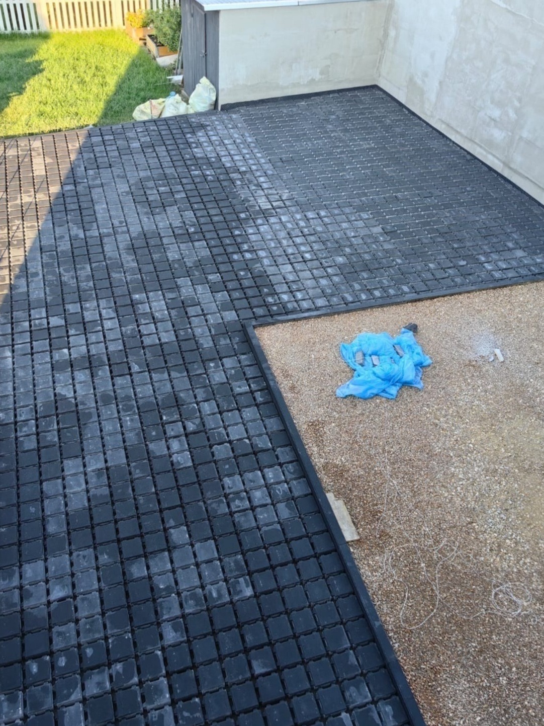 Montaż ażurowych płyt na podbudowie z kruszywa, widoczne przygotowane podłoże i fragment trawnika w tle.