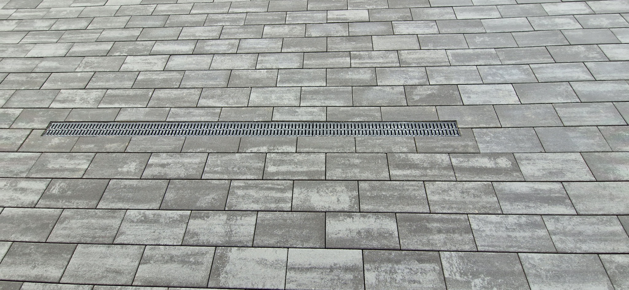 Ułożona szara kostka brukowa z liniowym odpływem wody pośrodku kadru.