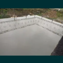 Świeżo wylana, gładka powierzchnia jastrychu na balkonie z ozdobną, metalową balustradą, odbijającą się w mokrej posadzce.