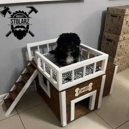 Brodaty stolarz Michał Pajek - Pies rasy pekińczyk siedzi wewnątrz drewnianego, dwupoziomowego domku dla zwierząt z białymi balustradami i schodkami, obok widoczne logo firmy z narzędziami.