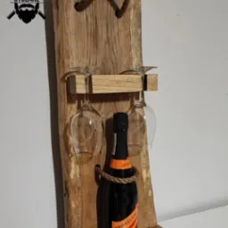 Drewniany stojak na wino i kieliszki z butelką prosecco, zawieszony na ścianie, z widocznym logo firmy w lewym górnym rogu.