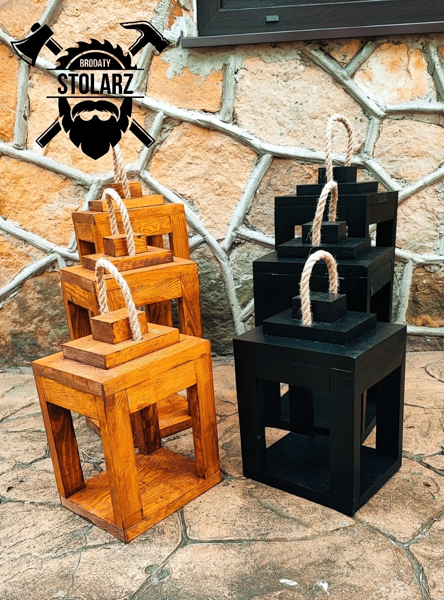 Ręcznie wykonane drewniane lampiony w kolorze naturalnego drewna i czarnym, ustawione na zewnątrz na tle kamiennej ściany, z logo firmy w górnej części kadru.