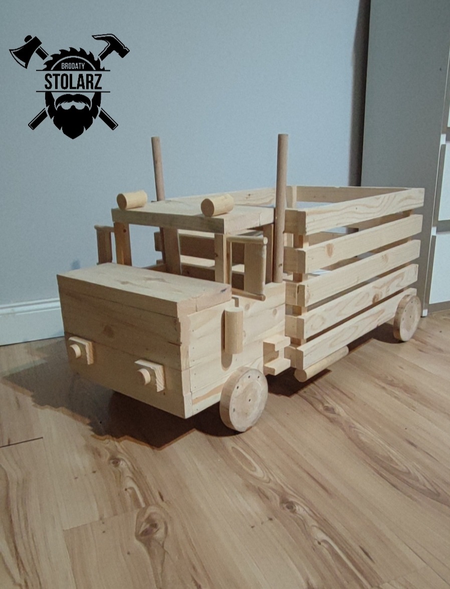 Ręcznie wykonany model ciężarówki z jasnego drewna, złożony z desek i okrągłych elementów, z logo firmy na ścianie w tle.