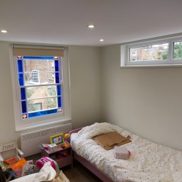 Daniel Demkowski - Pokój dziecięcy z łóżkiem z motywem gwiazdek, kolorowym oknem z niebieskimi akcentami i wbudowanym oświetleniem punktowym w suficie.