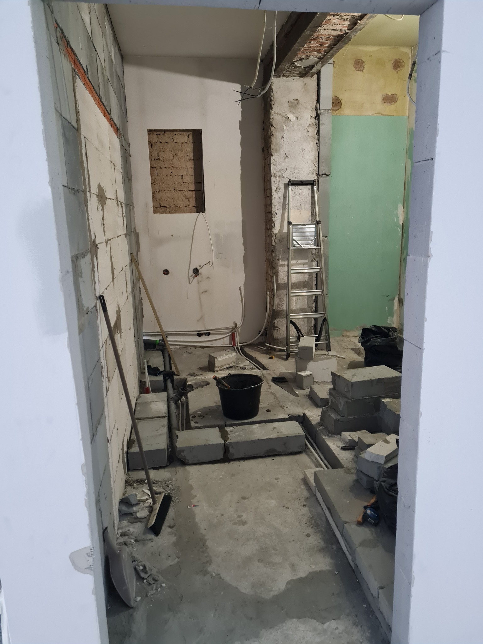 Wnętrze w trakcie demontażu ścian z widocznymi blokami betonowymi, instalacjami, drabiną i narzędziami, ukazujące etap przygotowawczy do dalszych prac wykończeniowych.