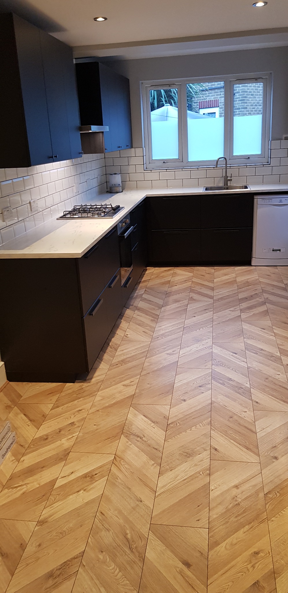 Nowoczesna kuchnia z ciemnymi szafkami, białym blatem i podłogą ułożoną w jodełkę, widok z perspektywy podłogi.