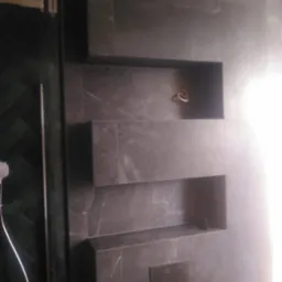 Łazienka wykończona ciemnoszarą płytką imitującą marmur, z wnękami w ścianie i widocznym panelem sterowania spłuczką.