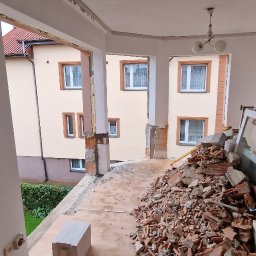 Do Usług Andrzej Ziółkowski Usługi Ogólnobudowlane - Demontaż balkonu: sterta gruzu ceglanego na balkonie z widokiem na budynek mieszkalny, stare okna oparte o ścianę.