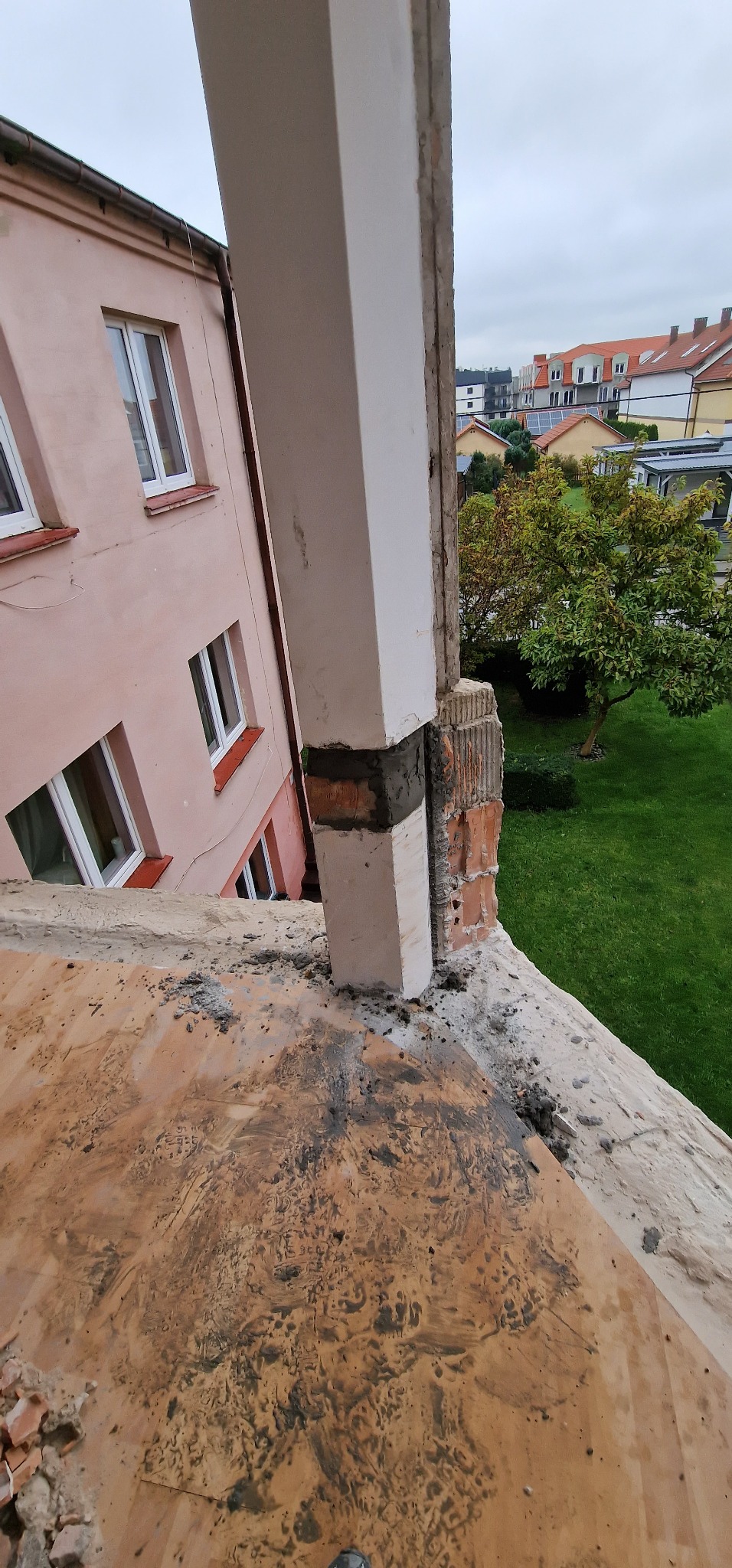 Wznoszenie filaru z cegieł i betonu na tle budynku z różową elewacją i zielonego trawnika