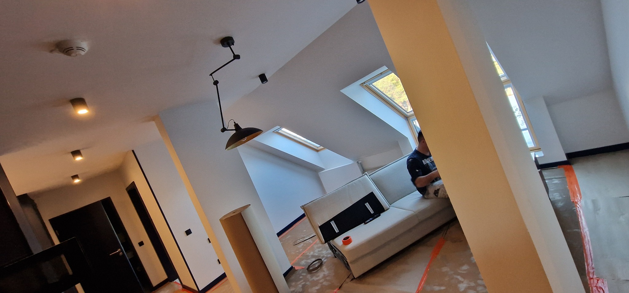 Montaż oświetlenia sufitowego w nowym, jasnym pomieszczeniu z oknami dachowymi i rozłożoną sofą.