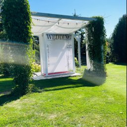 Myjnia parowa Legnica Wojciech Jurkiewicz - Plenerowa instalacja ślubna: biała altana z napisem 'Wedding Magazine', opleciona zielenią, na tle trawnika i drzew. Dekoracja na imprezę.