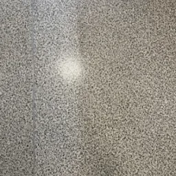 Szara podłoga z drobnym wzorem, widoczna fuga i delikatne odbicie światła.