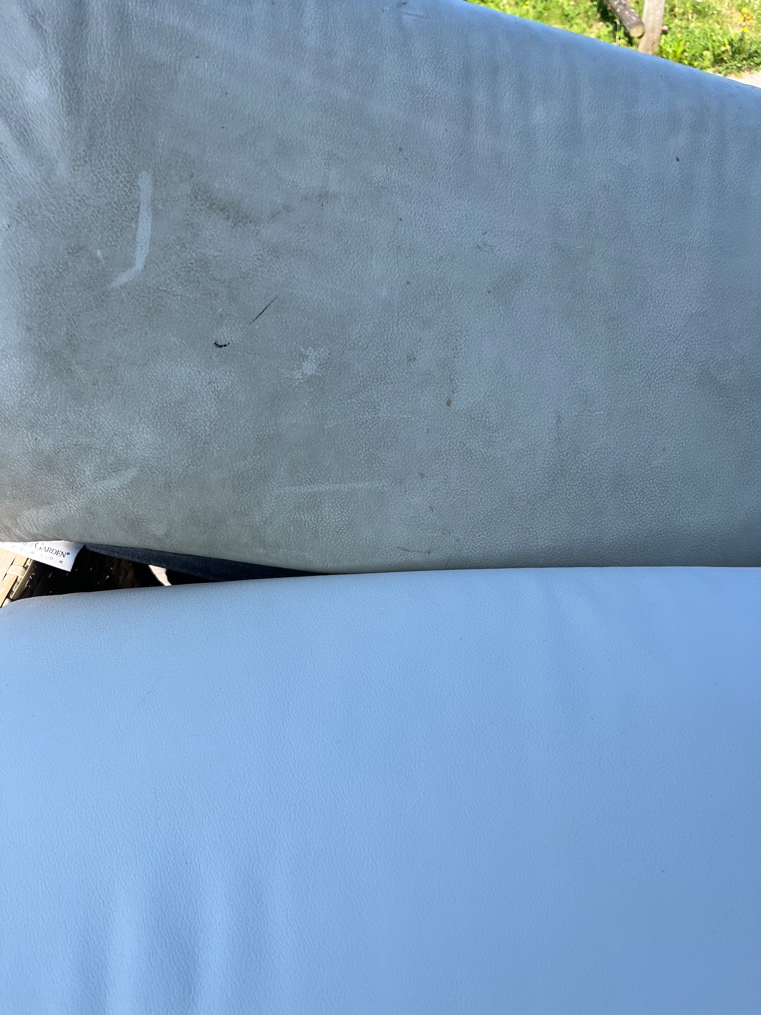 Porównanie dwóch fragmentów tapicerki meblowej: górny, kremowy, z widocznymi plamami i zabrudzeniami, oraz dolny, czysty, jasnoniebieski, o wyraźnej fakturze skóry.