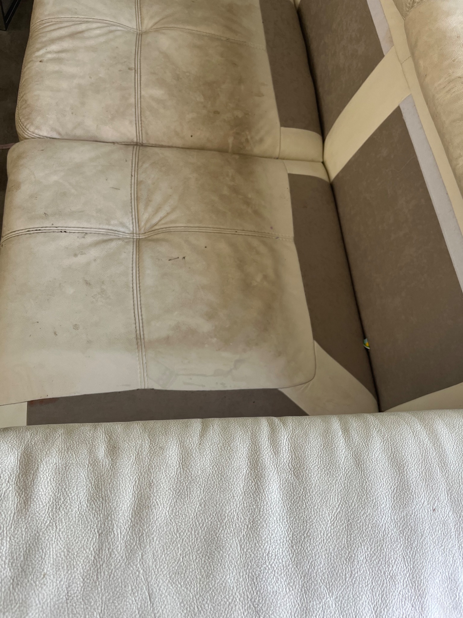 Brudna, jasna skórzana sofa z widocznymi plamami i zabrudzeniami na siedzisku i oparciu.