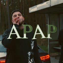 Michał Kapłanow mkvid media - Ujęcie z planu filmowego: mężczyzna z papierosem na tle auta i przystanku autobusowego z osobami. Duży napis 'APAP' nałożony na obraz.