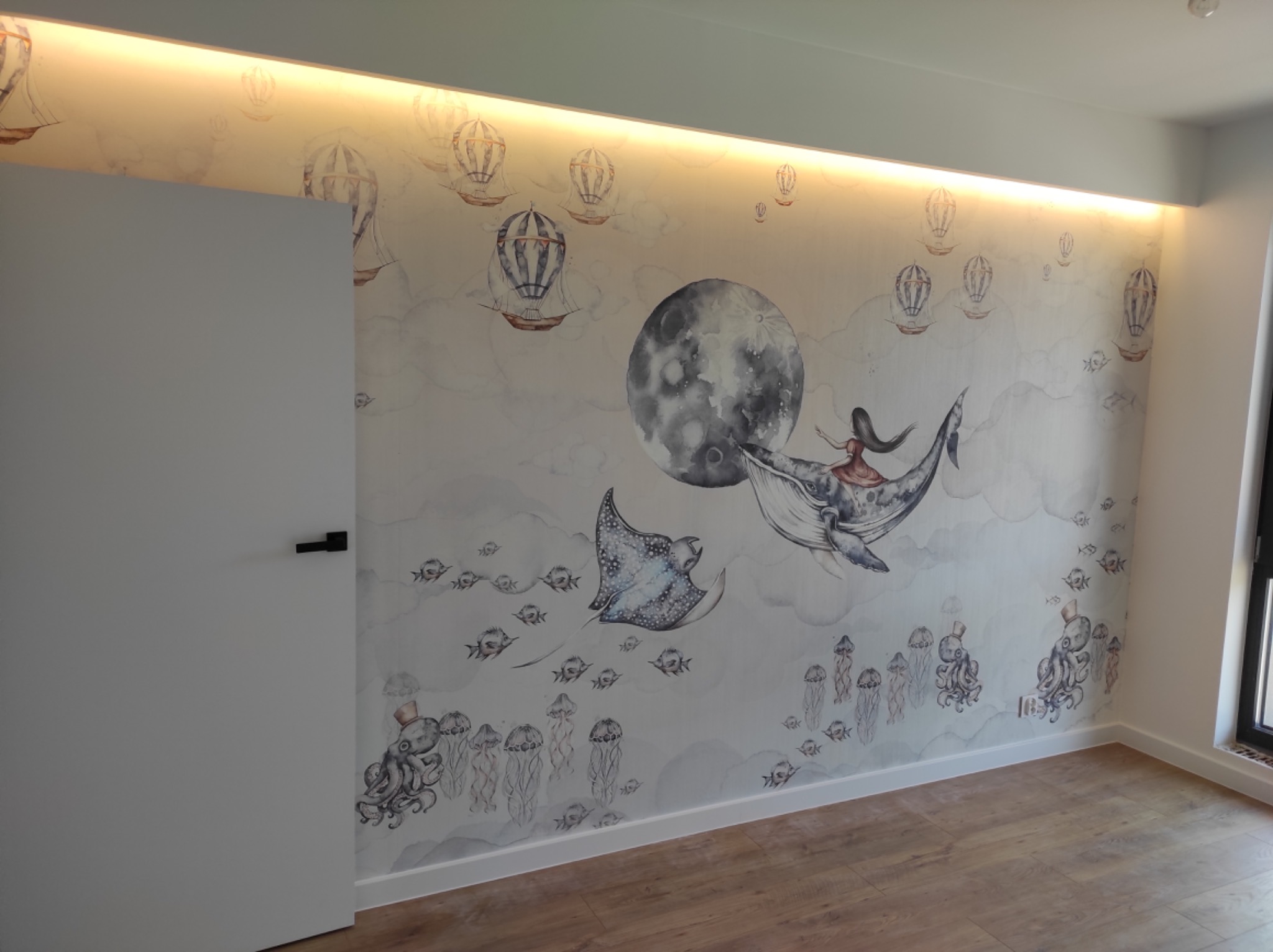 Pokój dziecięcy z fototapetą przedstawiającą motywy morskie i balony na tle księżyca, oświetlenie LED ukryte w suficie, drewniana podłoga, białe listwy przypodłogowe i drzwi.
