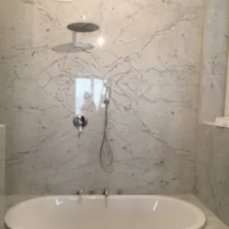 Elegancka łazienka z wanną i marmurowymi płytami ściennymi z wyraźnym wzorem żyłkowania, deszczownica zamontowana na suficie, bateria wannowa czterootworowa.