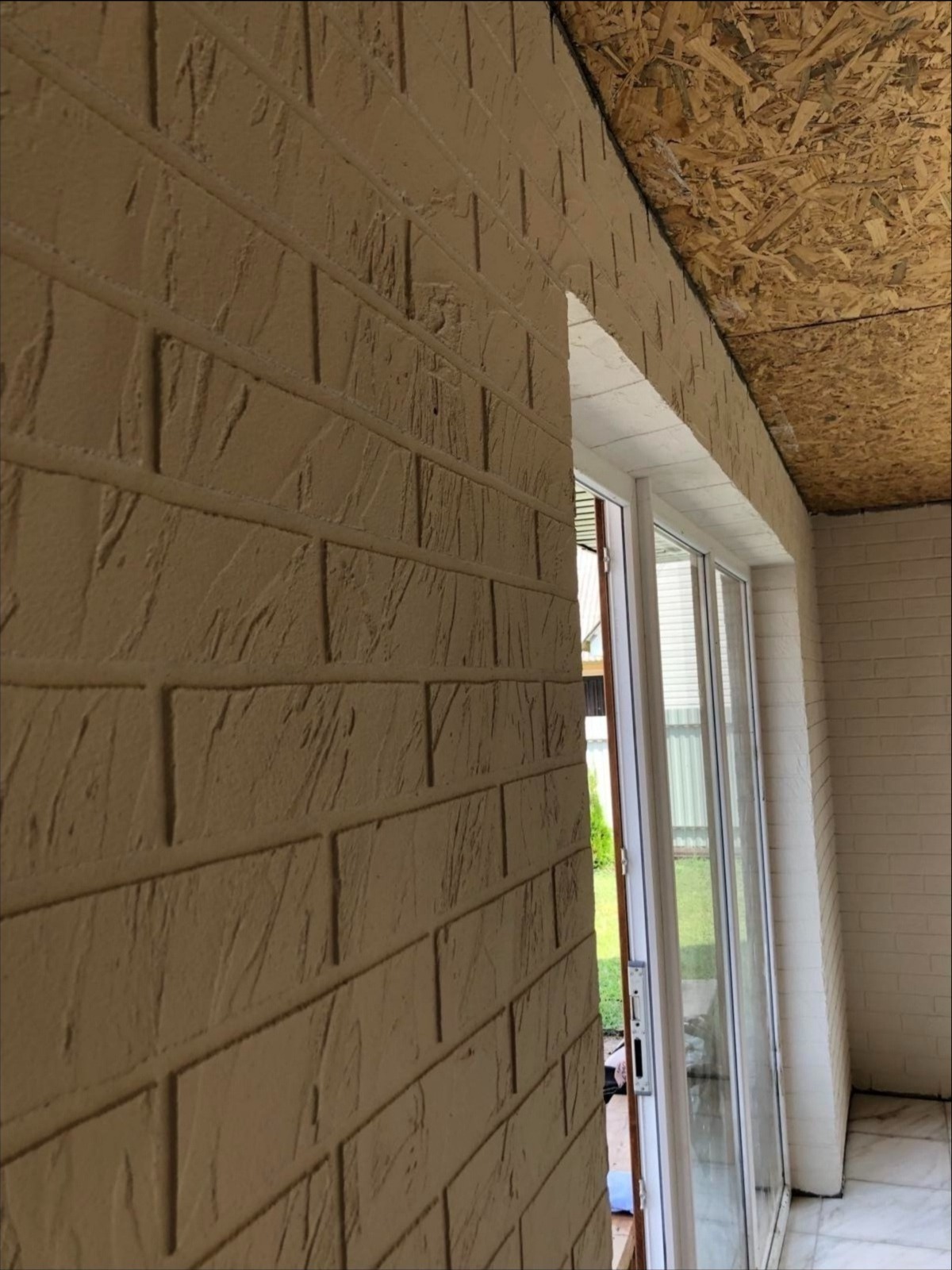 Wykończona elewacja budynku z imitacją cegły, widoczna z bliska pod kątem, z oknem przesuwnym i fragmentem drewnianej konstrukcji dachu.