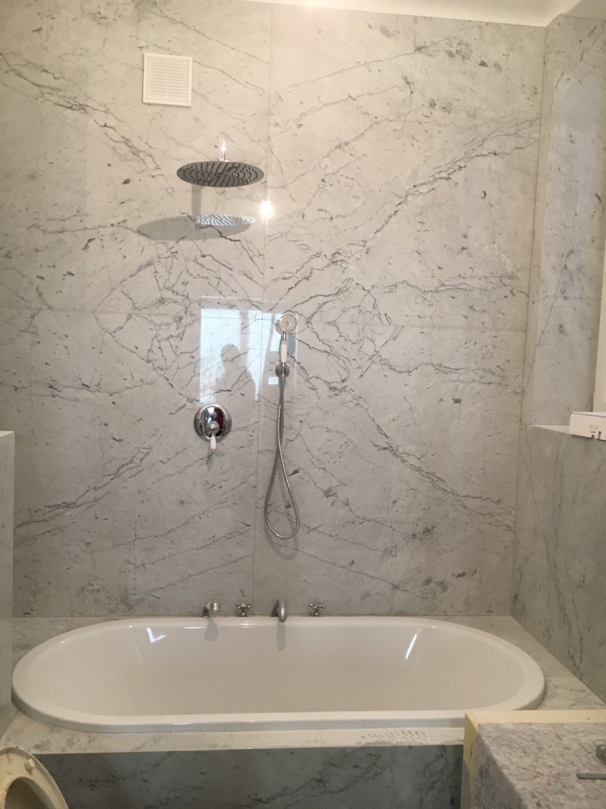 Elegancka łazienka z wanną i marmurowymi płytami ściennymi z wyraźnym wzorem żyłkowania, deszczownica zamontowana na suficie, bateria wannowa czterootworowa.