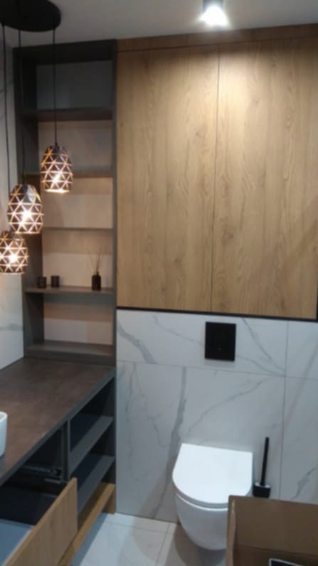 Nowoczesna łazienka z wiszącą toaletą, marmurowymi płytkami i drewnianymi szafkami. Oświetlenie punktowe i dekoracyjne lampy wiszące dodają elegancji.