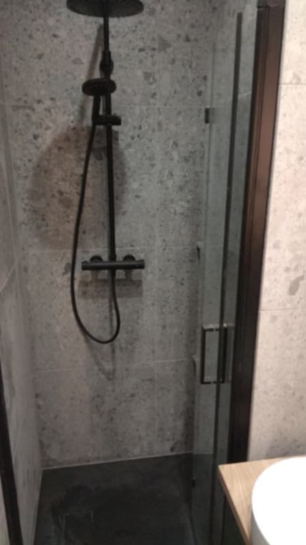 Nowoczesna kabina prysznicowa z deszczownicą w odcieniach szarości. Czarna armatura i ciemna podłoga kontrastują z jasnymi płytkami. Minimalistyczny design.