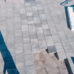 Szara kostka brukowa w trakcie układania, widoczny fragment podsypki piaskowej i poziomica w tle.