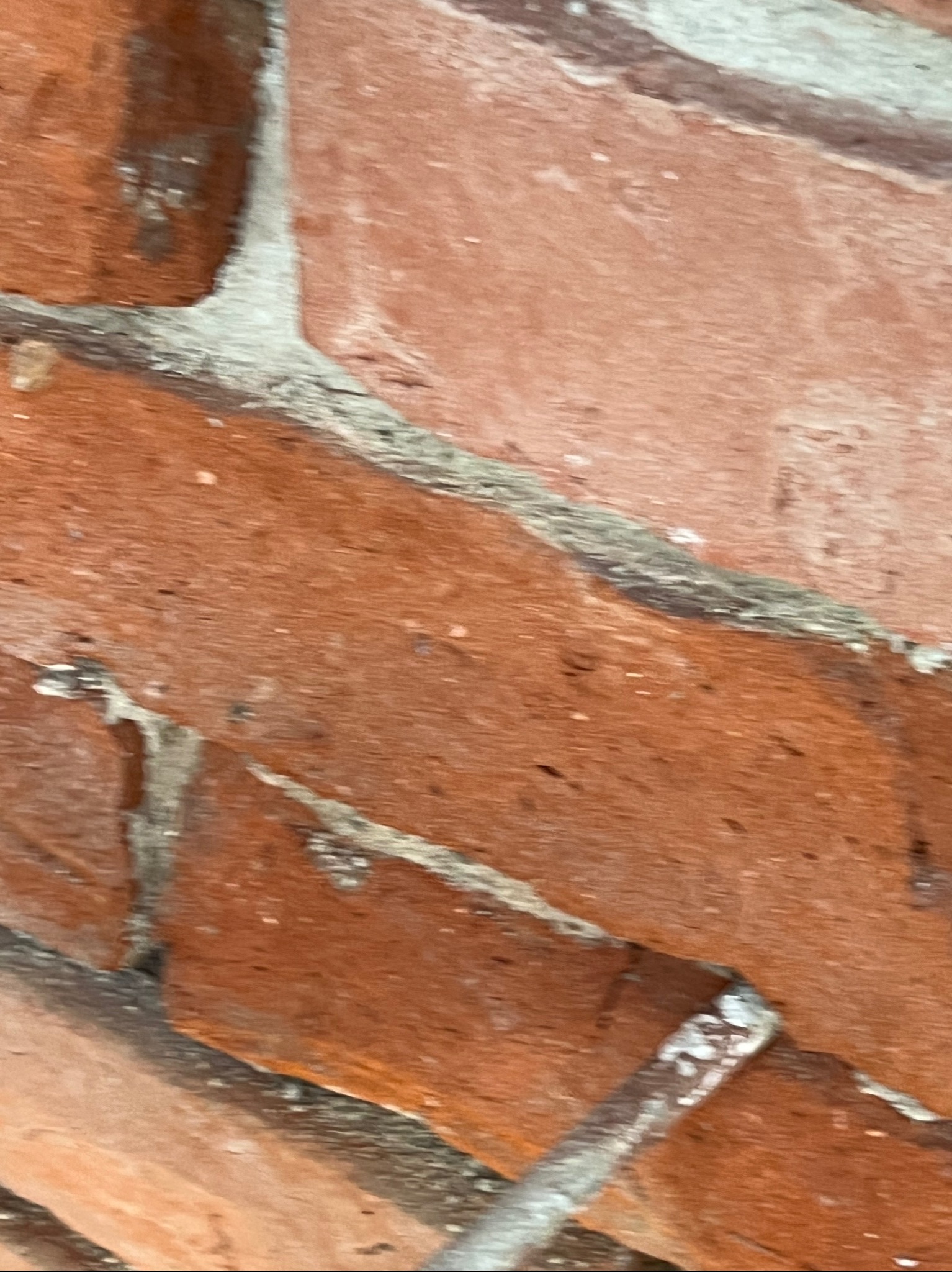 Fragment ściany z czerwonej cegły, z widocznymi spoinami wypełnionymi zaprawą. W dolnej części kadru widoczny element narzędzia do spoinowania.