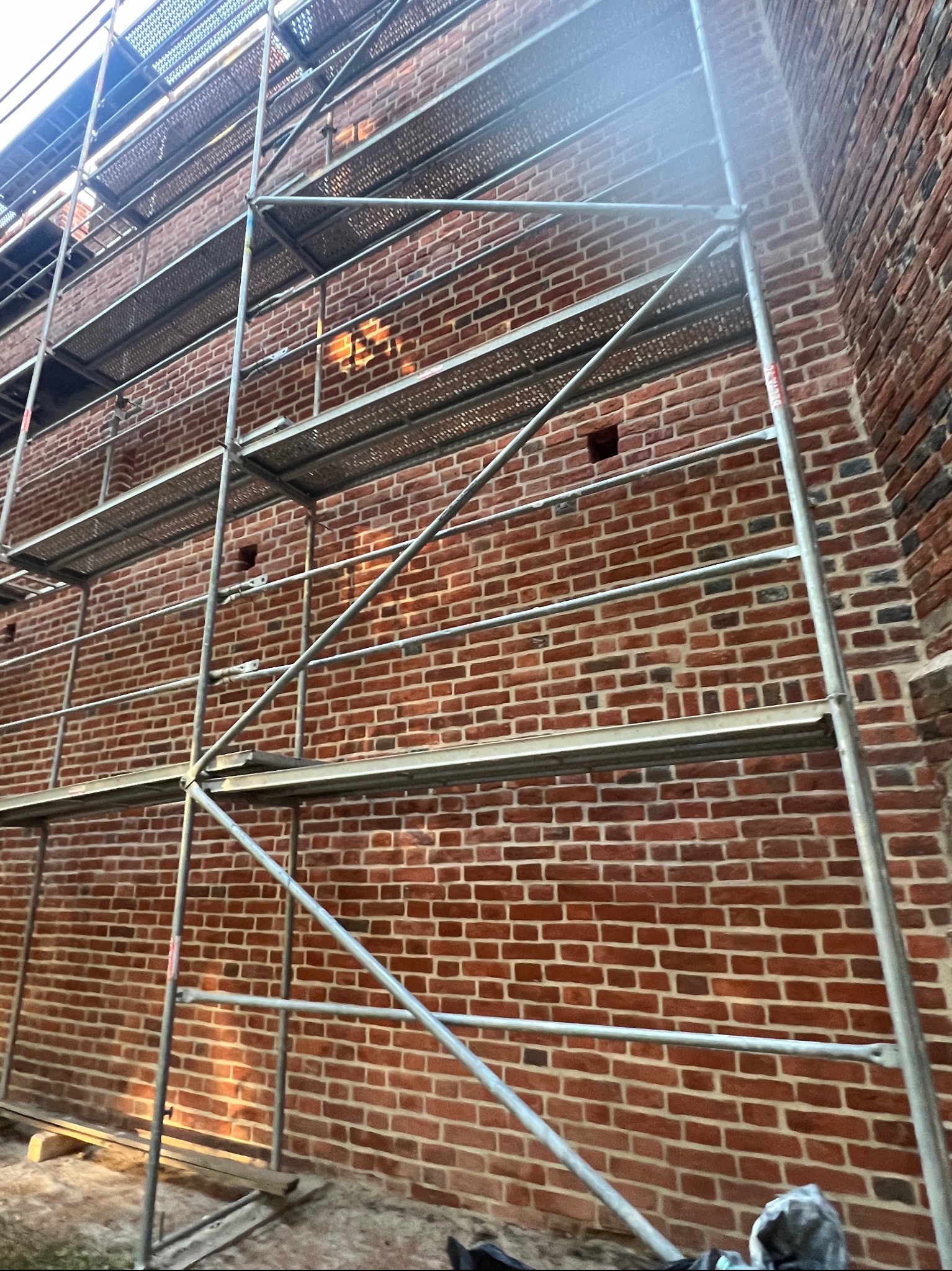 Ceglana ściana zabytkowej kamienicy w trakcie renowacji, osłonięta rusztowaniem. Widoczne detale muru i konstrukcji rusztowania, perspektywa z dołu.