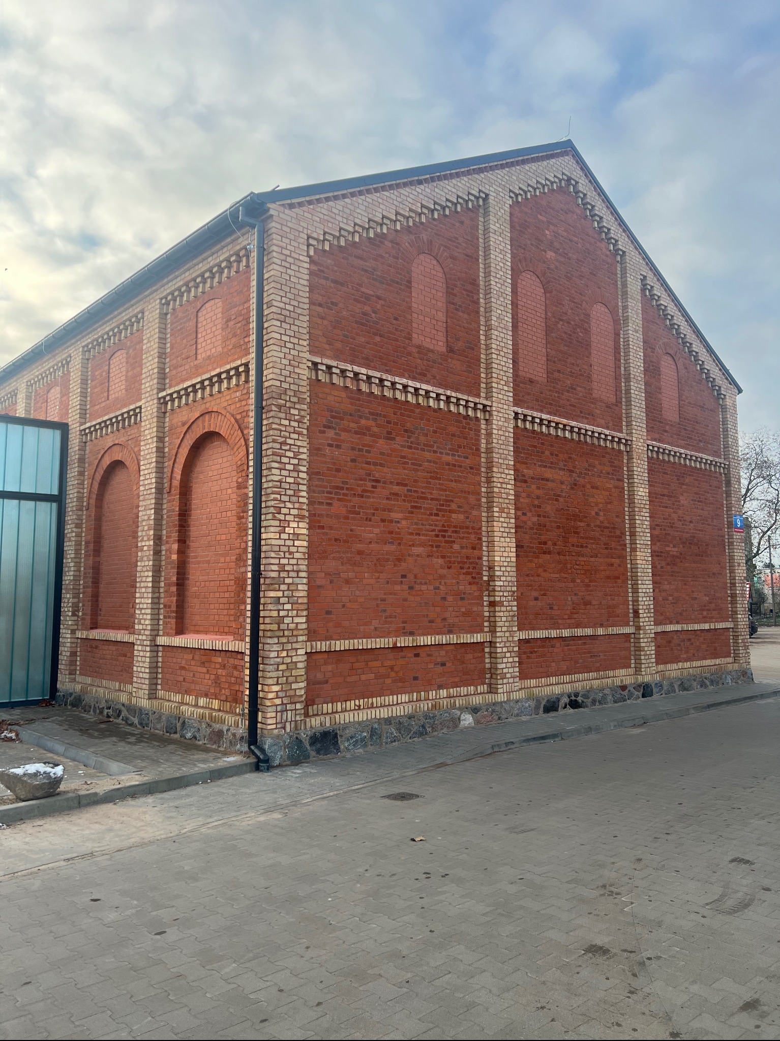 Ceglany budynek z dekoracyjnymi elementami z jasnej cegły, widoczny z poziomu ulicy w pochmurny dzień. Budynek po renowacji elewacji.