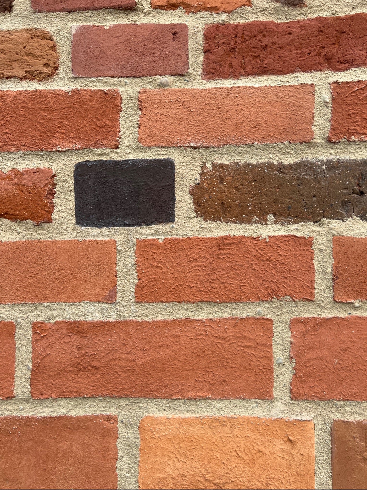 Ceglana ściana z fugami, gdzie jedna cegła jest czarna, a pozostałe w odcieniach czerwieni i brązu. Tekstura cegieł i fug jest wyraźnie widoczna.