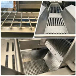 Wnętrze przemysłowej maszyny ze stali nierdzewnej z różnymi elementami: rusztem, perforowaną powierzchnią, oraz zestawem ostrzy. Widoczne detale konstrukcyjne, takie jak śruby i spawane łączenia.