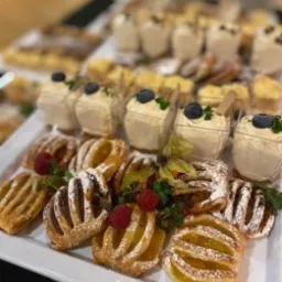 Elegancko ułożone na białej tacy słodkie przekąski w Gdańsku: mini desery w przezroczystych pojemnikach z borówkami i listkami mięty, obok kruche ciasteczka z owocowym nadzieniem posypane cukrem...