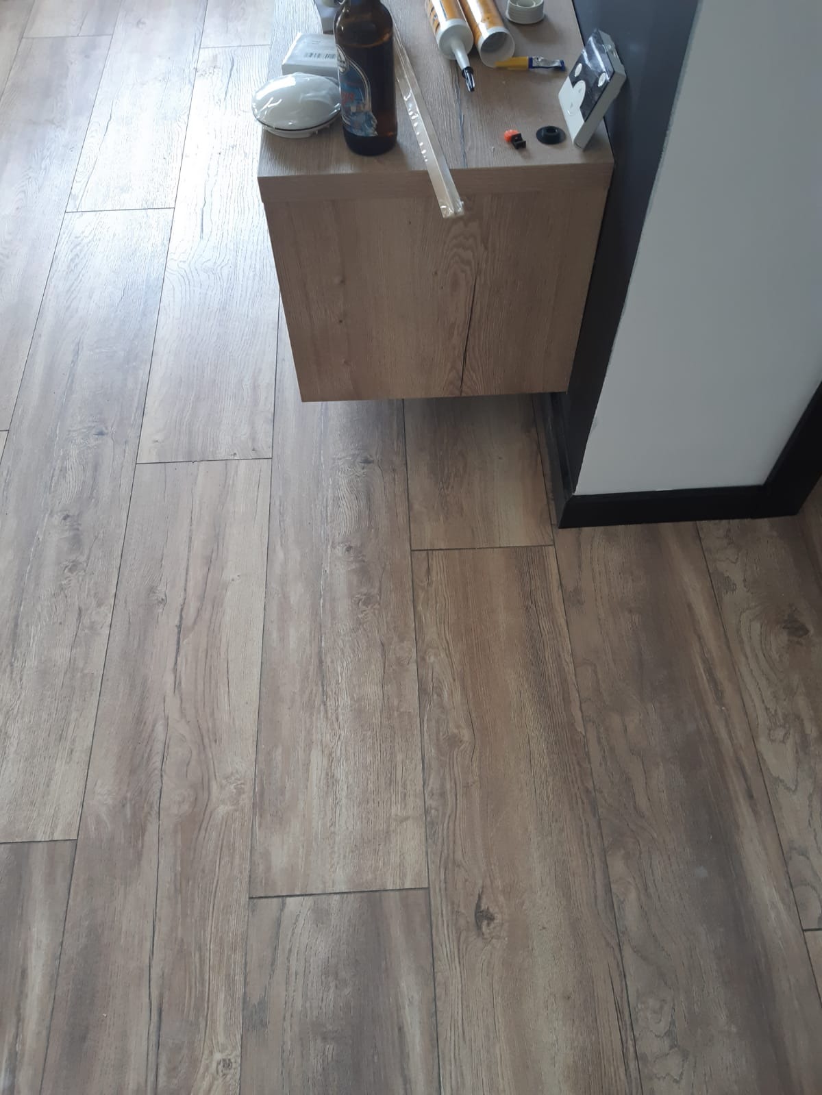 Świeżo położone panele podłogowe z widoczną deską pod umywalkę i narzędziami pracy oraz napojem.