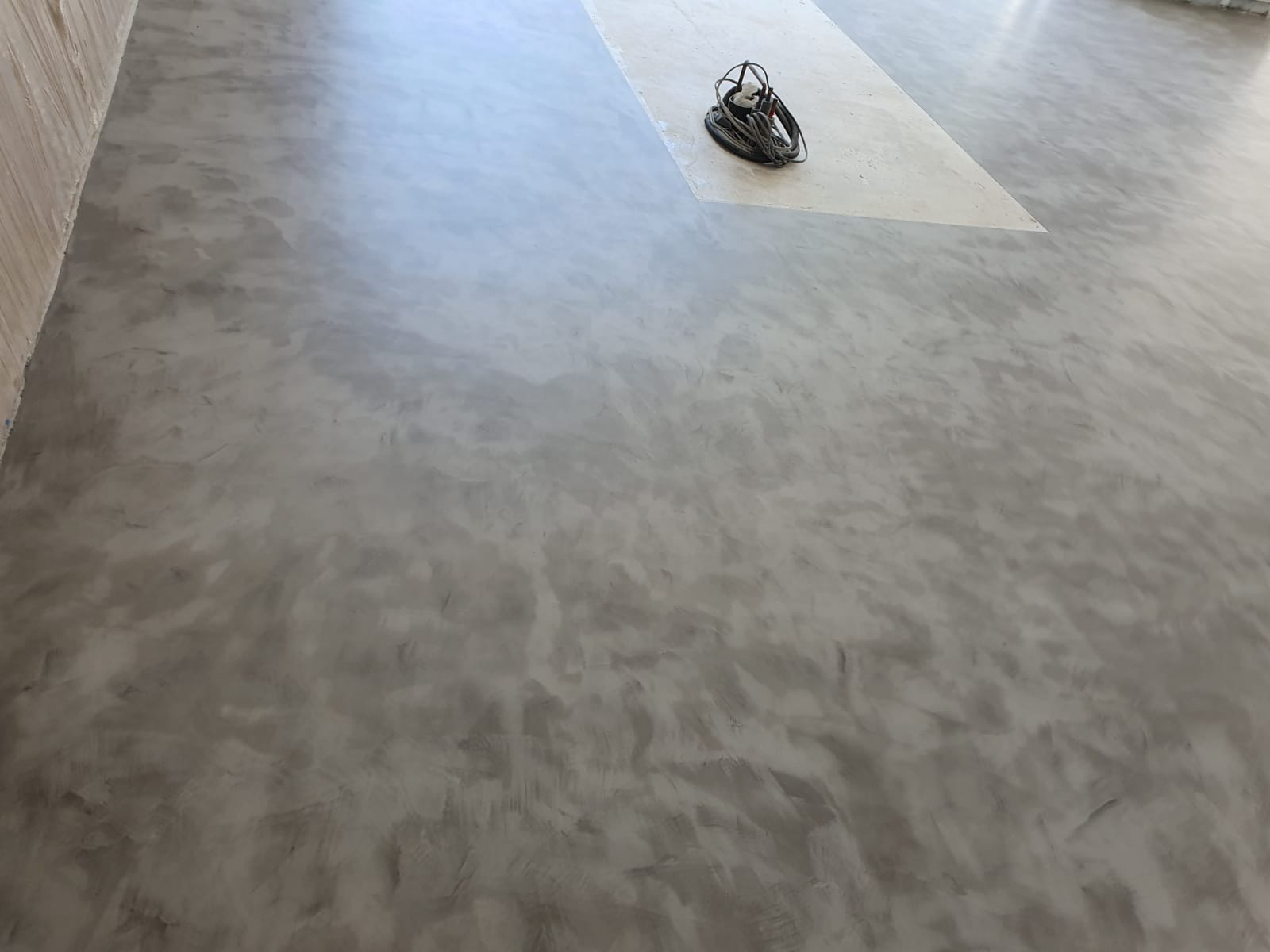 Szara, betonowa podłoga z efektem dekoracyjnym, na jasnym tle leży zwinięty kabel elektryczny.