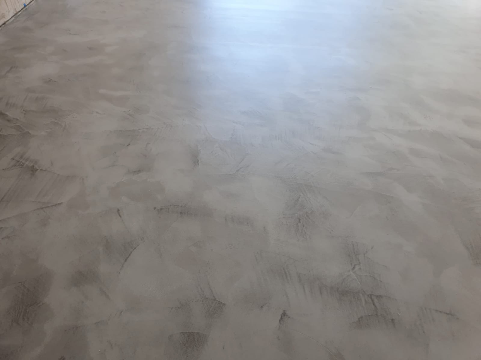 Świeżo położona, szara, dekoracyjna warstwa wykończeniowa na podłodze, z widocznymi śladami pędzla i delikatnym połyskiem w górnej części kadru.