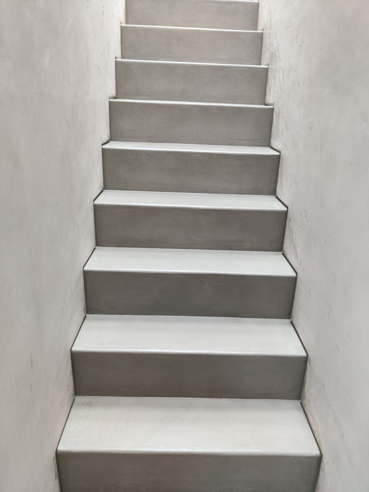 Schody wewnętrzne wykończone gładzią cementową, widok z dołu, szare stopnie i ściany z efektem betonu architektonicznego.