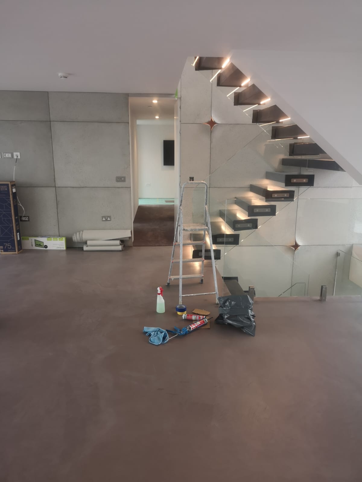 Wnętrze w trakcie prac wykończeniowych: widoczne ściany z paneli, nowoczesne schody z podświetleniem, drabina, oraz narzędzia i materiały budowlane na podłodze.