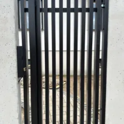 Nowoczesna, czarna furtka z pionowych profili zamontowana pomiędzy betonowymi słupkami w Białymstoku.