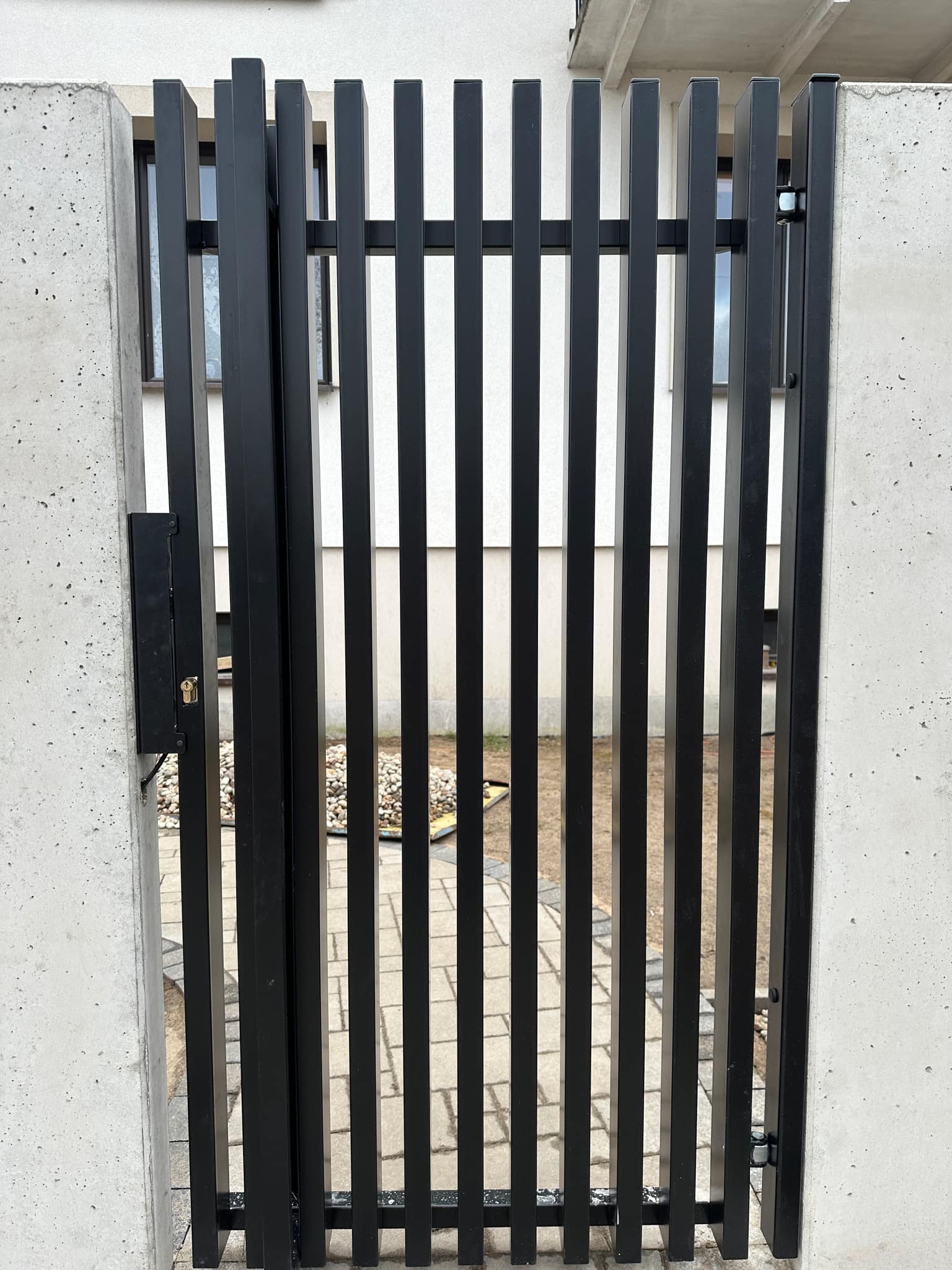 Nowoczesna, czarna furtka z pionowych profili zamontowana pomiędzy betonowymi słupkami w Białymstoku.