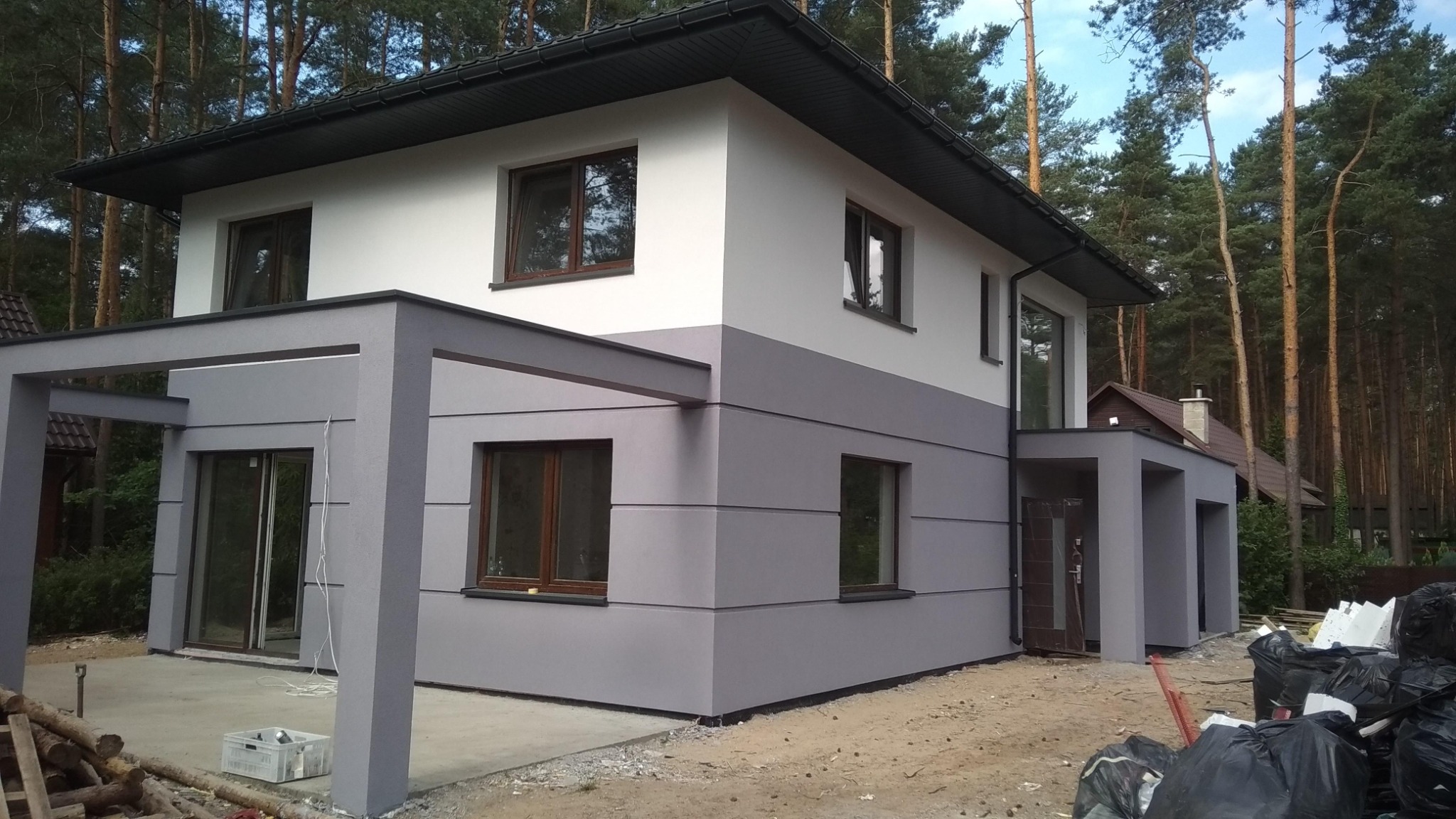 Dwukondygnacyjny dom jednorodzinny po renowacji elewacji w Łodzi, z szarą dolną częścią i białą górną, otoczony drzewami.