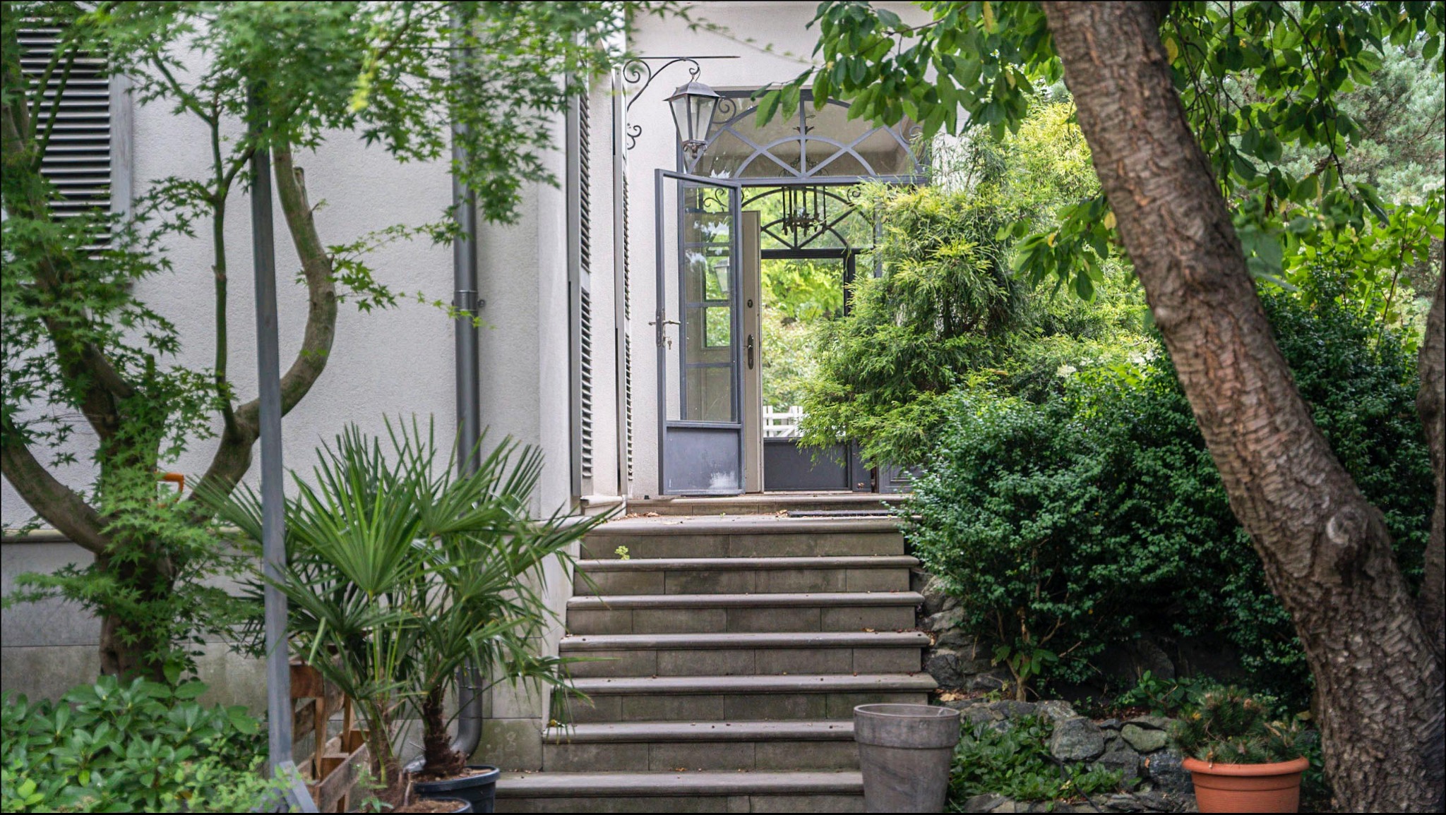 Wejście do domu w Łodzi z otwartymi drzwiami, schodami i bujną zielenią w ogrodzie.
