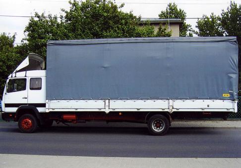 Biała ciężarówka z szarą plandeką zaparkowana na ulicy, widok z boku, czerwone felgi.