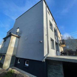 ELTAR Konrad Lamprecht - Odnowiona elewacja budynku wielorodzinnego w odcieniach szarości, z widocznym fragmentem balkonu i klimatyzatorem na ścianie, uchwycona w słoneczny dzień z perspektywy żabiej