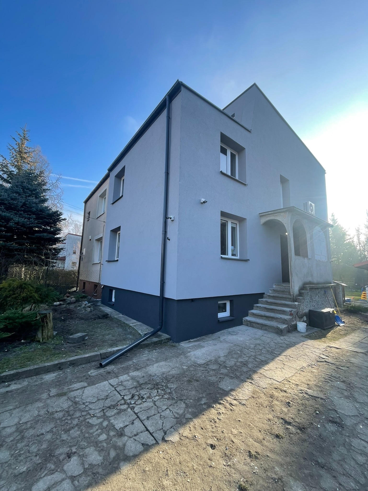 Odnowiony budynek w Kobyłce z elewacją w odcieniach szarości, widoczne nowe okna PCV i odświeżone schody wejściowe z elementami do wykończenia.