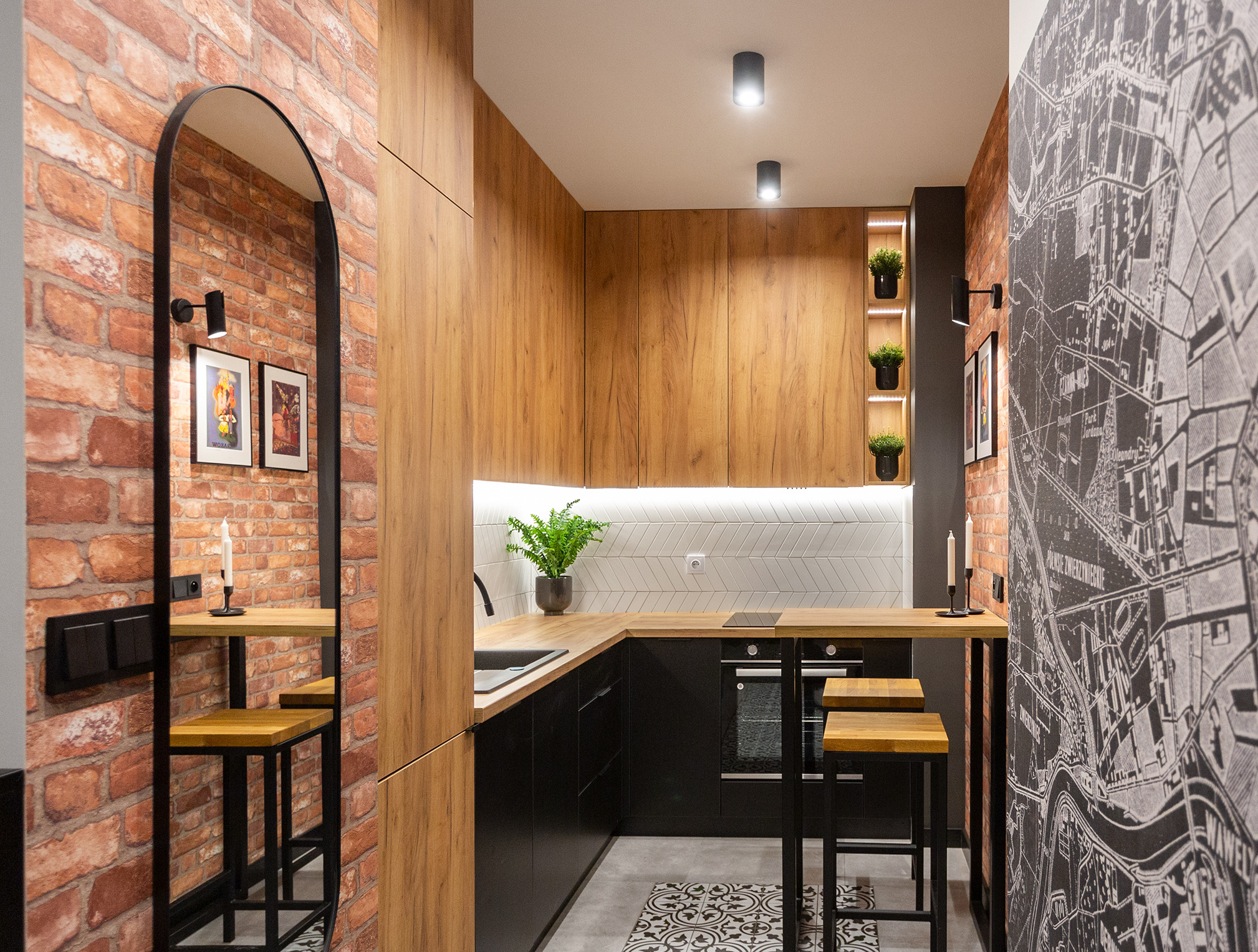 Nowoczesna kuchnia z ceglaną ścianą, drewnianymi szafkami i czarnymi elementami, wzorzysta podłoga i mapa miasta na ścianie, lustro z widocznym fragmentem baru