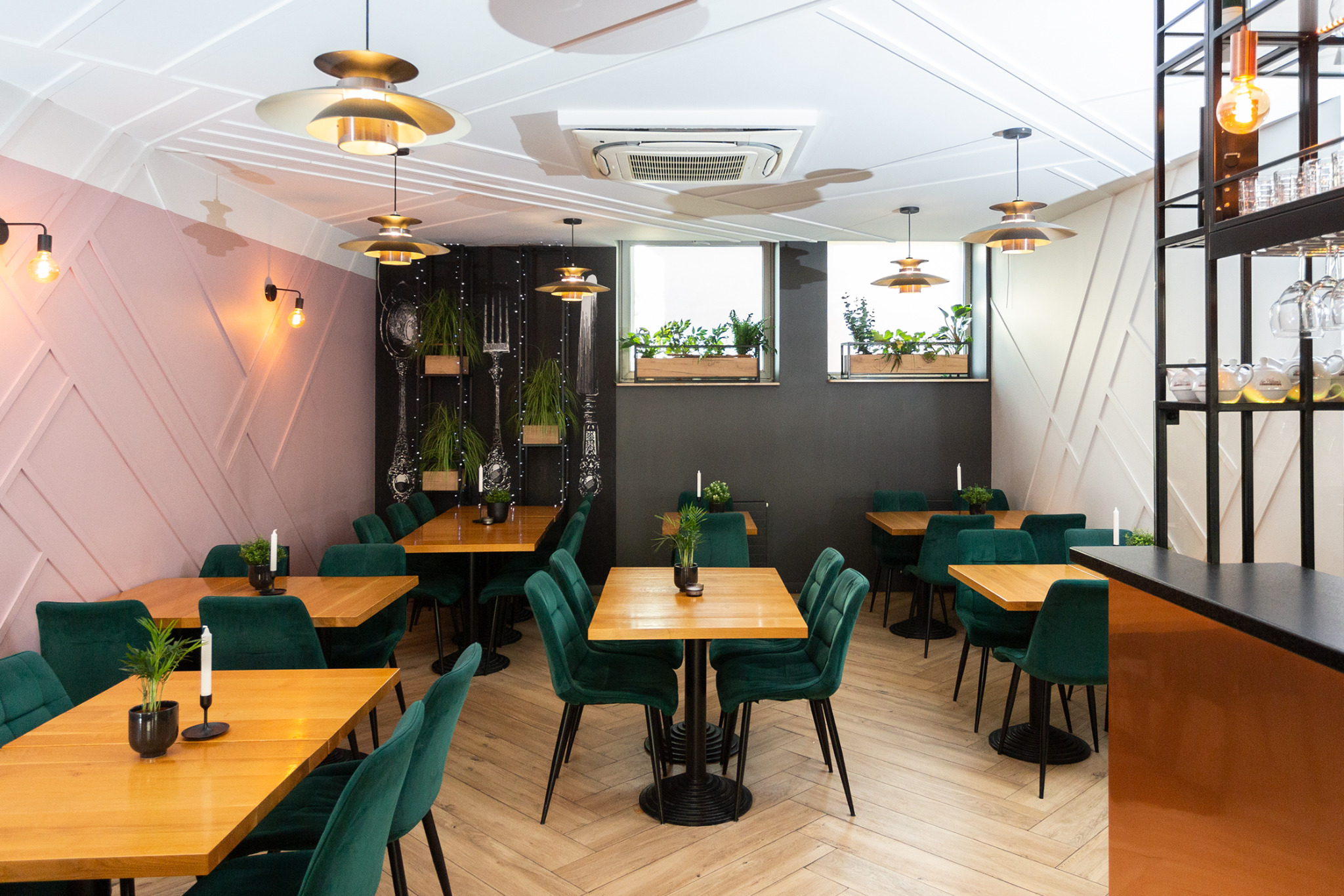 Wnętrze restauracji w Siemianowicach Śląskich z drewnianymi stołami, zielonymi krzesłami z aksamitu, dekoracyjnymi sztućcami na ścianie i roślinami w oknach.