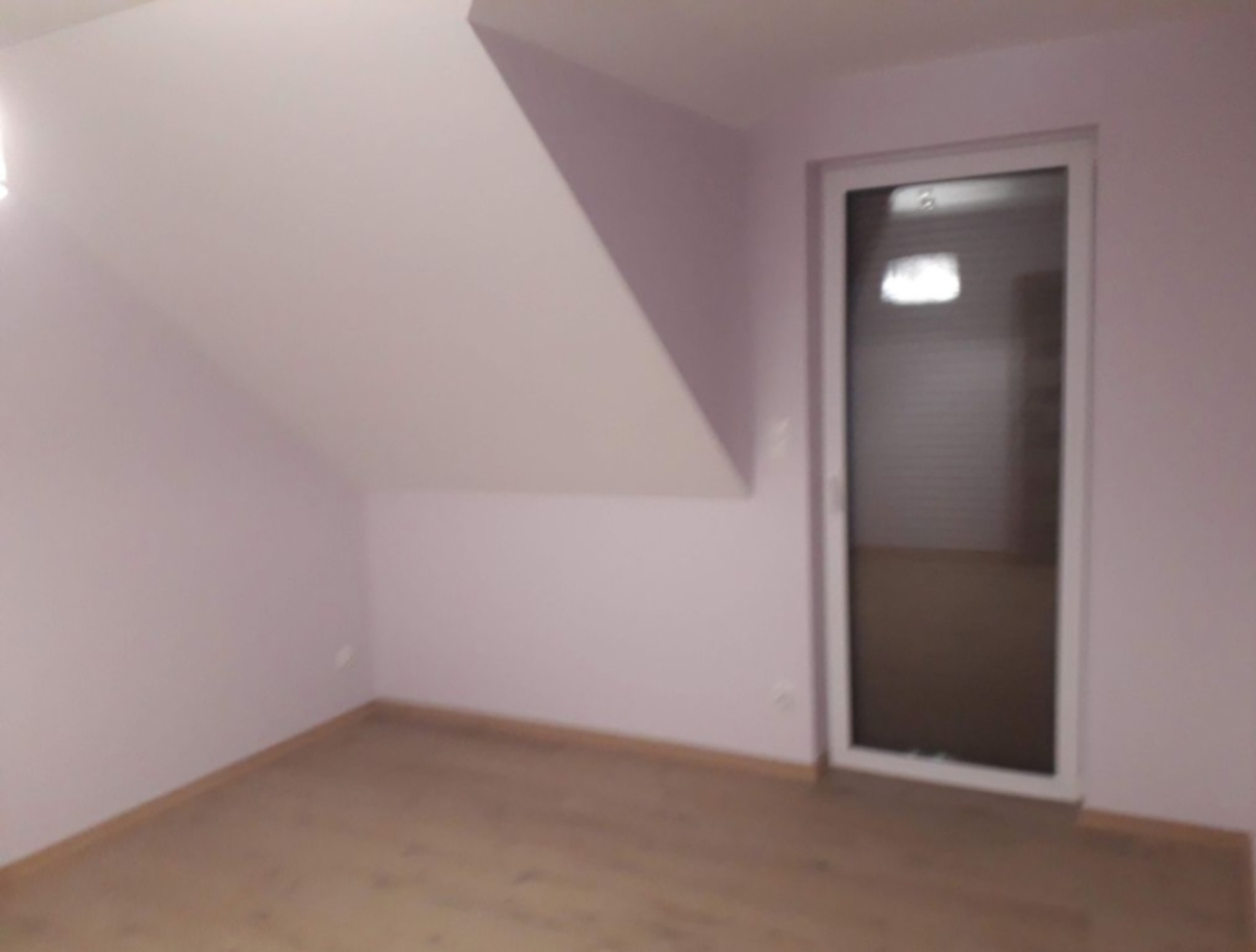 Poddasze po remoncie z jasnymi ścianami, drewnianą podłogą i białymi drzwiami balkonowymi.