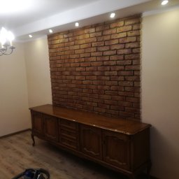 Usługi Budowlane Michał Hiller - Salon z dekoracyjną ścianą z cegły, oświetleniem punktowym i antycznym kredensem z ciemnego drewna.